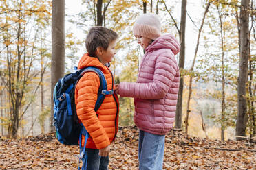 sister helps brother fasten his backpack - ELMF00159