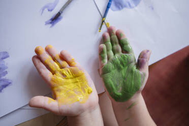 child of preschool age painting with paints at a table at home. child's palms stained with yellow and green paint close-up - KVBF00084