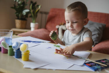 Portrait of a child of preschool age painting with paints at a table at home. Child puts a handprint on a sheet - KVBF00085