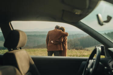 couple of elderly man and woman hugging on meadow in the mountains, view from a car. Sudetes, Poland - VSNF01790