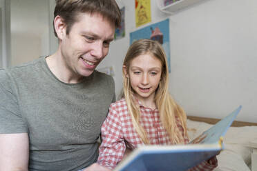 A father man with European appearance is reading book to his daughter 9 years old girl in pyjama - NJAF00925