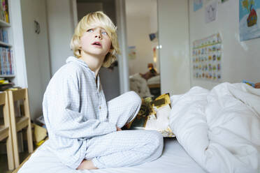 A 6 years old boy in blue pyjama is sitting on the bed - NJAF00935