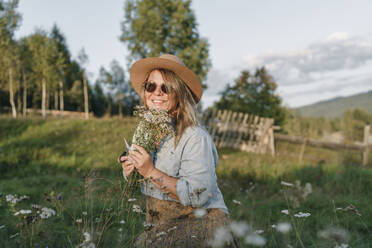 Woman collects flowers and herbs in a field - VBUF00533