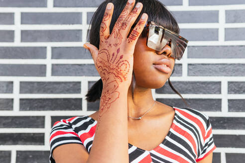 Close up of black woman's hand adorned with intricate henna designs, complementing her chic sunglasses and urban style - ADSF54413