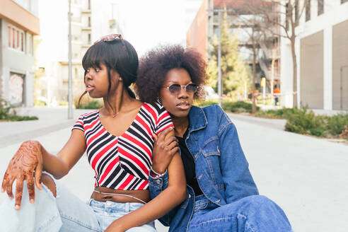 Two sisters share a moment on a city sidewalk, their casual styles and relaxed postures capturing the essence of urban life - ADSF54415