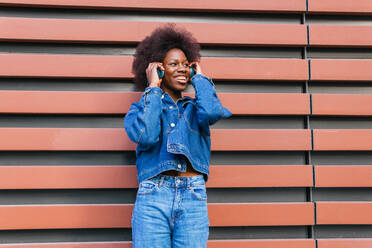 A radiant woman enjoys her favorite tunes, dressed head to toe in classic denim against a geometric terracotta backdrop - ADSF54431