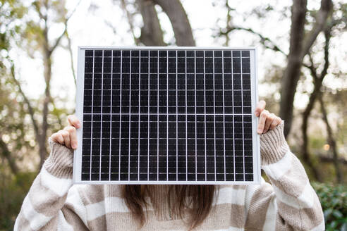 A person obscured by a solar panel stands among trees, representing eco-friendly energy. - ADSF54460