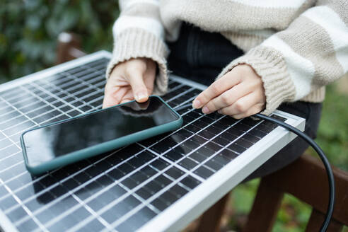 Close-up of a person's hands charging a smartphone using a portable solar panel. - ADSF54462