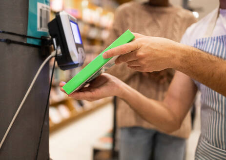 A cropped anonymous person's hands are shown paying with a card at a card reader during the checkout process at a grocery store - ADSF54468