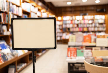 An empty black signage board stands prominently in a warmly lit bookstore filled with shelves of various books, inviting customization with messages or advertising. - ADSF54489