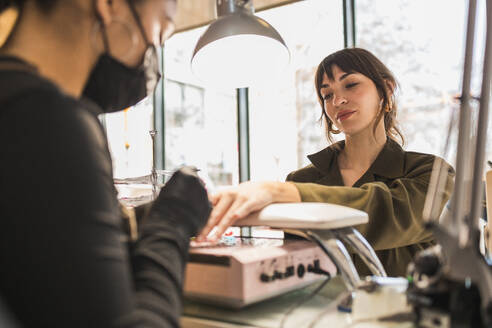 A woman receives a manicure at a stylish salon, with a focus on her hands under a lamp - ADSF54493