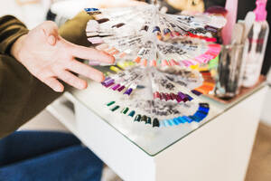 A person's hand is selecting from a variety of nail polish color samples displayed in a fan arrangement at a salon - ADSF54494