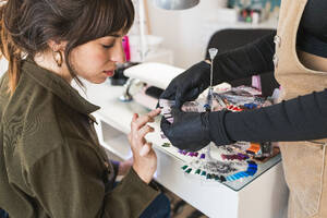 A woman selecting from a variety of nail polish color samples displayed in a fan arrangement at a salon - ADSF54497