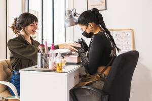 Smiling customer receives a manicure from a masked nail technician at a salon - ADSF54498