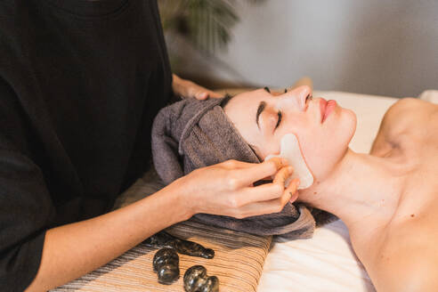 An individual enjoying a calming facial treatment involving massage and skin care at a serene spa setting - ADSF54501