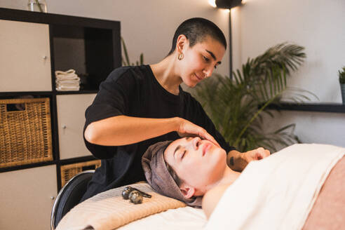 A focused beautician performs a facial massage on a client, emphasizing a serene spa experience - ADSF54503