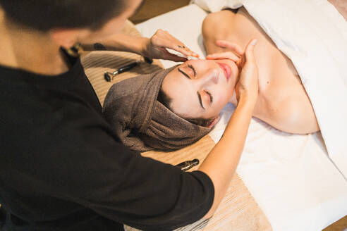 A therapist performs a gentle facial treatment on a relaxed client at a wellness spa, promoting skincare and relaxation - ADSF54504