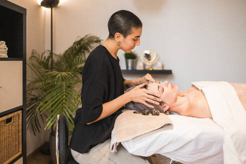 A professional therapist performs a relaxing facial massage on a client in a tranquil, contemporary spa setting, enhancing wellness - ADSF54505