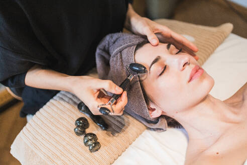 Serene woman receiving a calming facial massage with a jade roller in a tranquil spa setting, promoting relaxation and skincare - ADSF54506