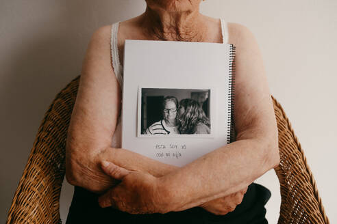 Elderly person holding a photo album close to their heart, featuring an image of them with a loved one - ADSF54514