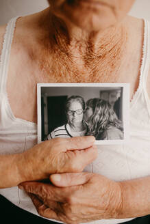 An elderly woman's hands cradle a photograph capturing a tender kiss on the cheek, evoking memories and emotions - ADSF54515