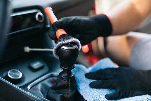 Close-up of hands wearing gloves cleaning a car's interior with a brush and cloth - ADSF54521