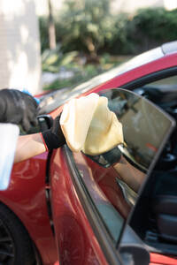 Close-up of a person's hands wiping a red car window with a yellow microfiber cloth - ADSF54523