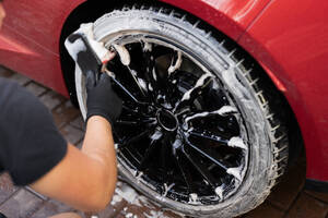 A person is meticulously cleaning a car tire with a foam brush, focusing on the details - ADSF54525