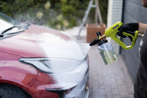 Person using a high-pressure foam lance to wash a red car, focusing on the car's front area - ADSF54526