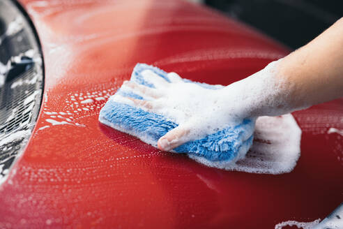 Hand washing a red car with a blue microfiber cloth and sudsy foam - ADSF54529