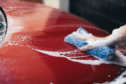 Close-up of a hand washing a red car with a soapy sponge, focusing on cleanliness and maintenance - ADSF54530