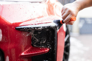 Hand washing a red car with detailer brush and soap suds on vehicle surface - ADSF54534