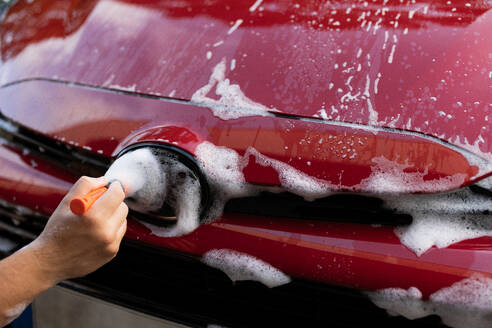 Hand washing a red car with soapy water and a sponge focusing on the details - ADSF54535