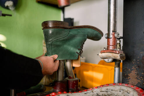 A skilled cropped unrecognizable shoemaker in Austria works on a green leather boot using traditional tools and techniques in their workshop. - ADSF54541