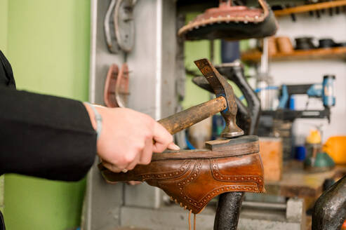 A cropped unrecognizable craftsman in Austria expertly hammers a shoe sole at a traditional shoemaking bench. - ADSF54543