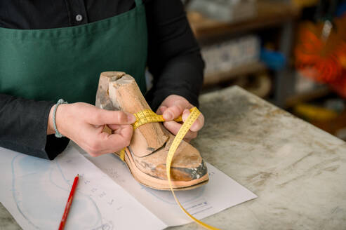 A cropped unrecognizable shoemaker in Austria measures a shoe last with a tape during the crafting process. - ADSF54549