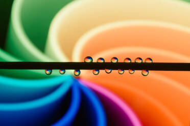 Vibrant water droplets poised on a thin rod reflect a spectrum of colors forming an abstract background. - ADSF54552