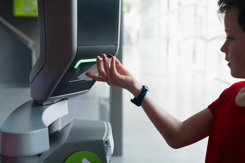 A young boy uses a ticket reading machine to access a science museum, symbolizing modern and interactive technology in educational environments. - ADSF54559