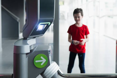 A young boy smiles as he uses a modern ticket reading machine at the entrance of a science museum, with a blurred girl in the background. - ADSF54560