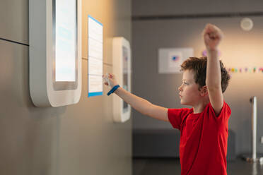 A curious boy in a red shirt reaches out to an interactive exhibit in a science museum, embodying the joy of learning. - ADSF54567