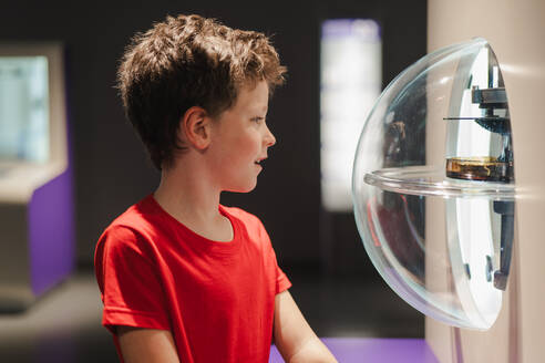 A young boy in a red shirt captivated by an interactive science exhibit, discovering the wonders of physics with earnest curiosity. - ADSF54570