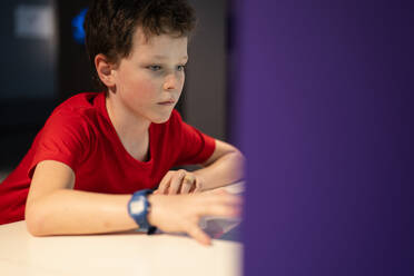 A young boy in a red shirt is focused while interacting with an exhibit at a science museum, embodying curiosity and education. - ADSF54573