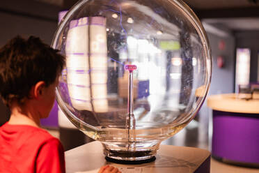 A young boy fascinated by a large plasma globe at a science museum, with his focus on the electrical arcs. - ADSF54574