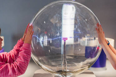 Boy and girl engaged with an interactive plasma globe exhibit at a science museum, showing curiosity and learning. - ADSF54579