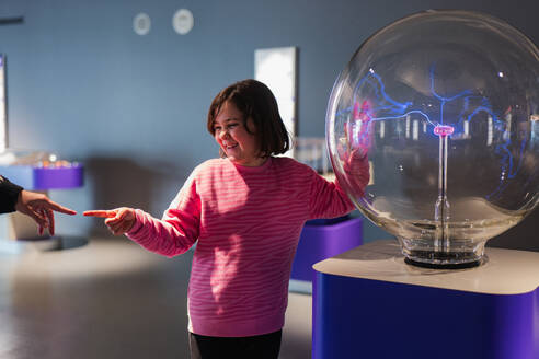Young girl enjoys a hands-on learning experience with a plasma globe at a science museum, showcasing curiosity and education. - ADSF54580