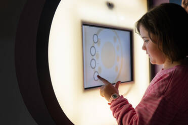 A girl in a pink shirt engages with a digital interactive display at a science museum, symbolizing education and curiosity in a technology-driven learning environment. - ADSF54582