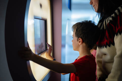 A boy and a woman engage with a touch screen at a science museum exhibit, displaying curiosity and learning. - ADSF54583