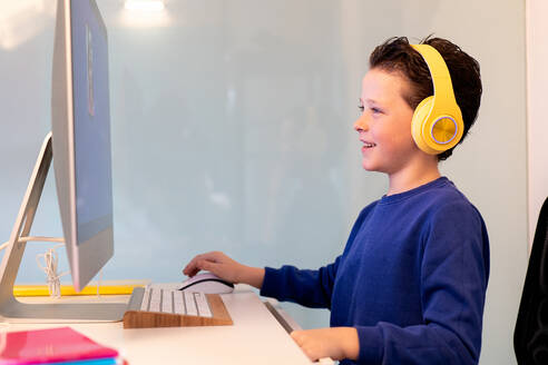 A cheerful child interacts with a computer, wearing bright yellow headphones, with a smile indicating enjoyment or success with the task at hand - ADSF54588