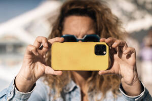 Eine Person mit markanten Händen, denen die Daumen fehlen, hält einen Moment mit einem Smartphone mit gelber Hülle fest; der Fokus der Kamera liegt auf dem angepassten Griff - ADSF54596