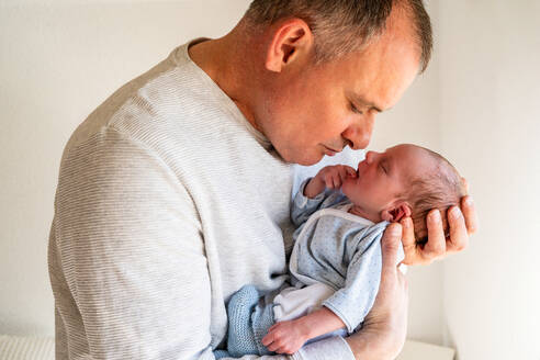 A loving father gently holds and gazes at his sleeping newborn baby, capturing a moment of paternal affection and care - ADSF54601